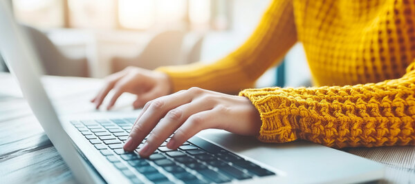 Im Bild bedient eine Person im orangenen Pullover einen Laptop. 